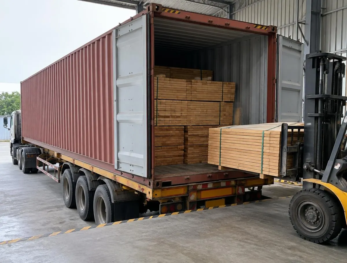 Shipping container being loaded with stacked timber at a warehouse dock